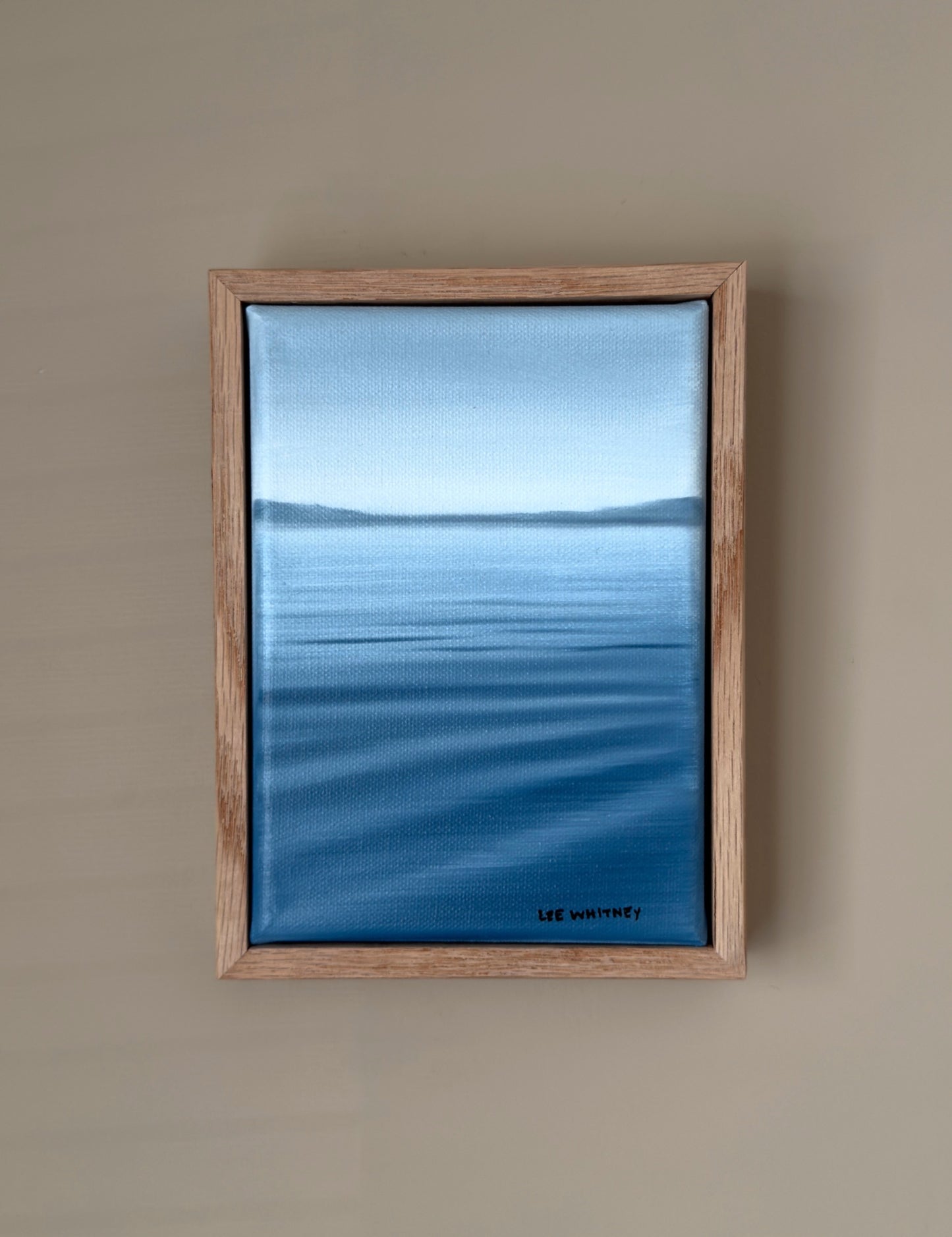 Framed artwork of a blue lakescape on a beige wall