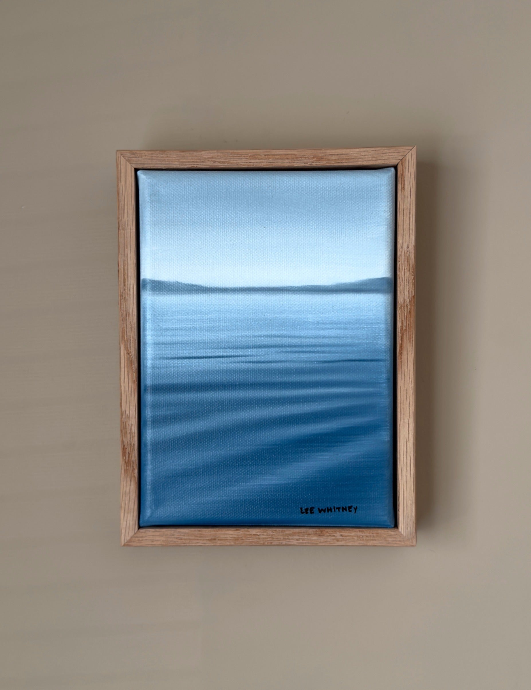 Framed artwork of a blue lakescape on a beige wall