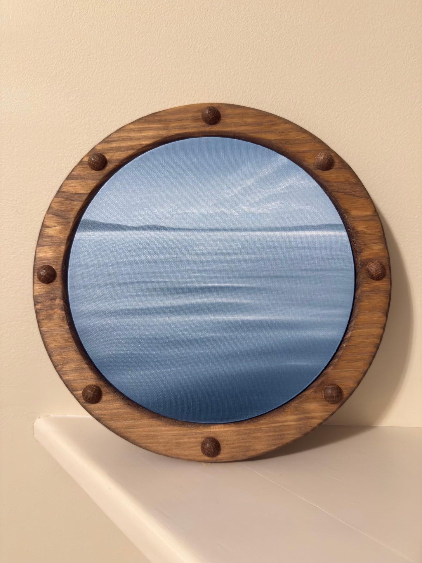 Light blue waterscape painting with porthole frame