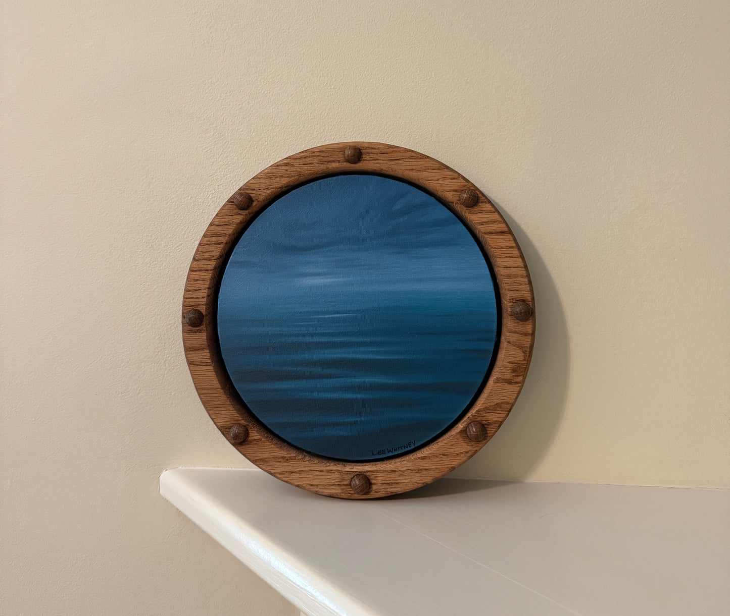 Round wooden-framed night waterscape painting on an off-white wall shelf
