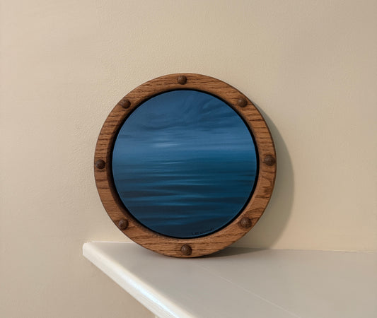 Round wooden-framed night waterscape painting on an off-white wall shelf