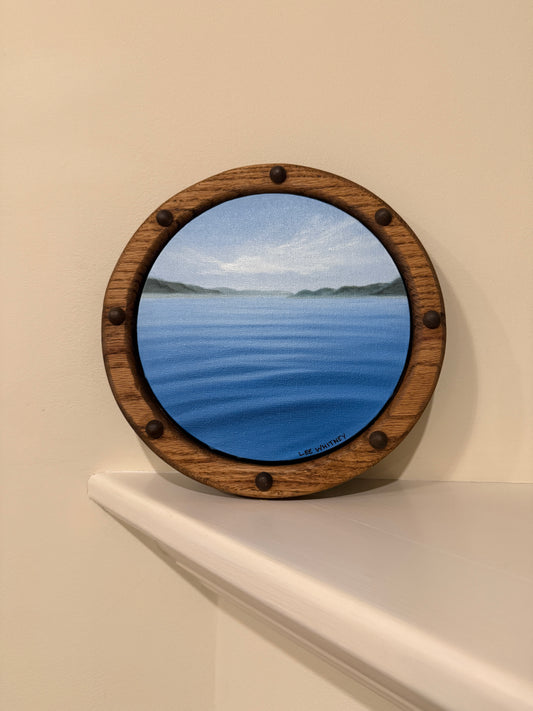 Round wooden framed waterscape painting on an off-white wall shelf