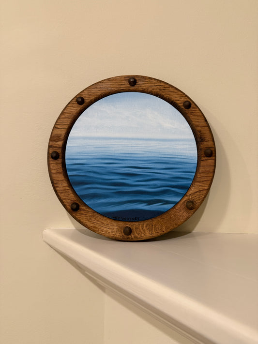 Wooden porthole frame on an off-white wall shelf with a blue ocean view painting