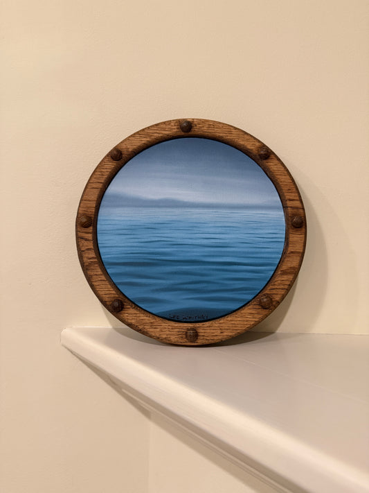 Round wooden-framed blue ripple waterscape painting on an off-white wall shelf