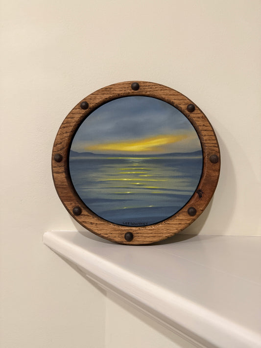 Round wooden frame with a sunset waterscape painting on an off-white wall shelf