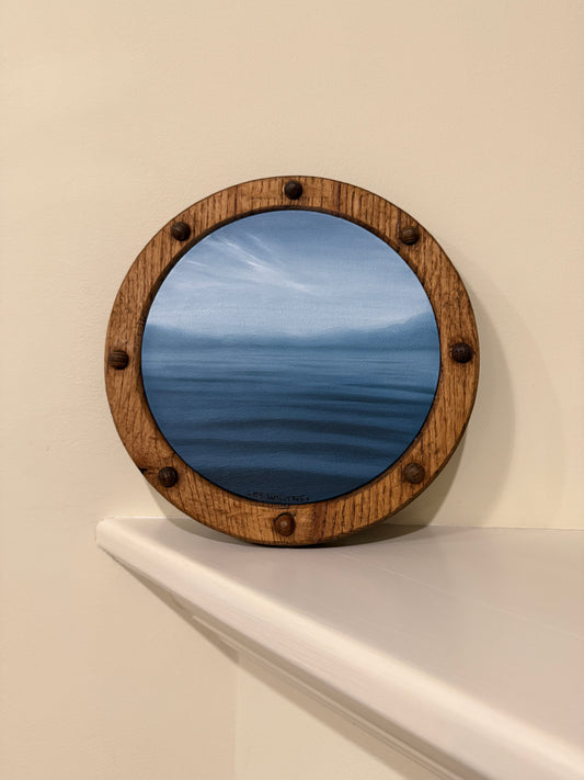 Round wooden-framed waterscape painting in slate blue on an off-white wall shelf