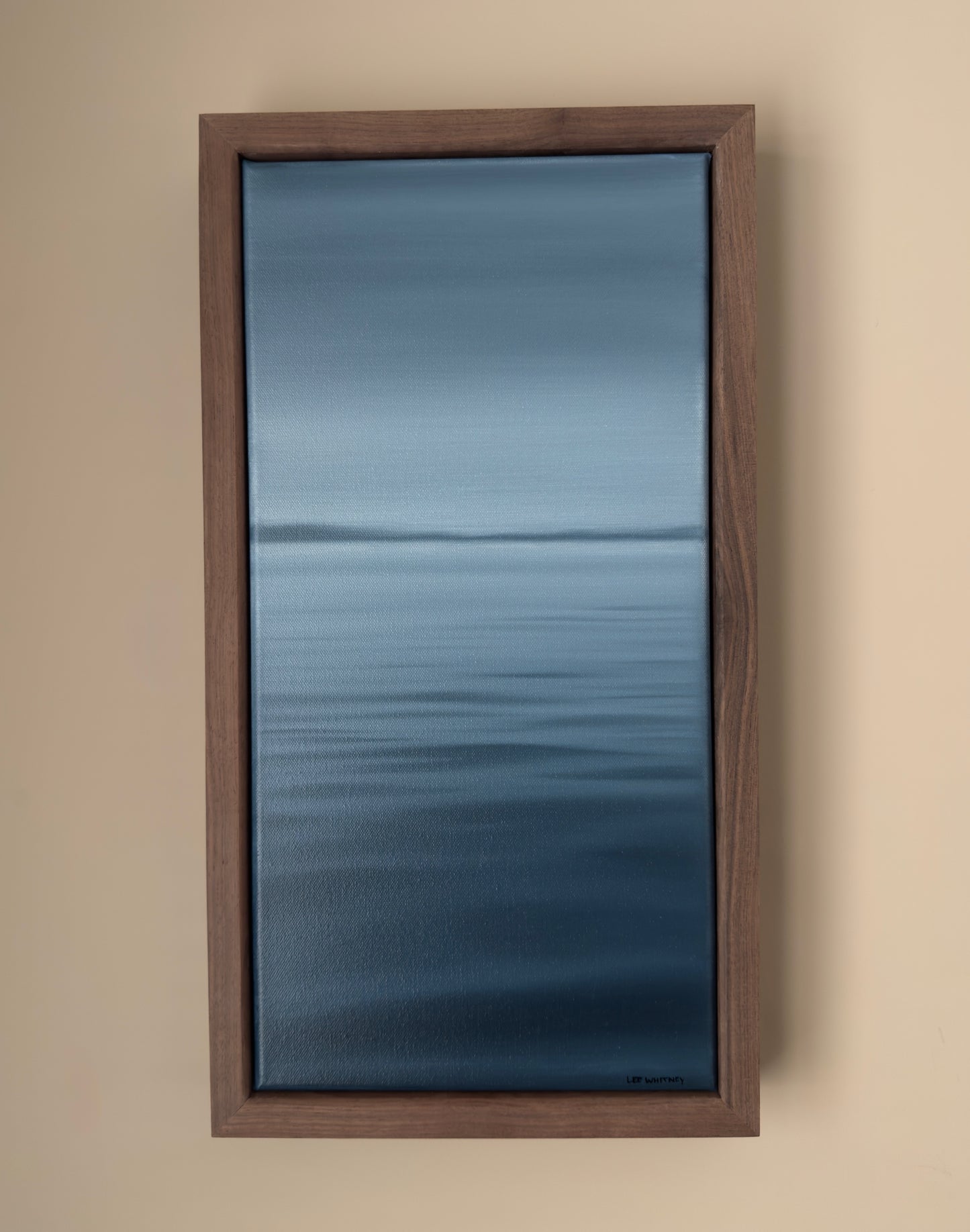 Framed artwork of a blue abstract waterscape on a beige wall