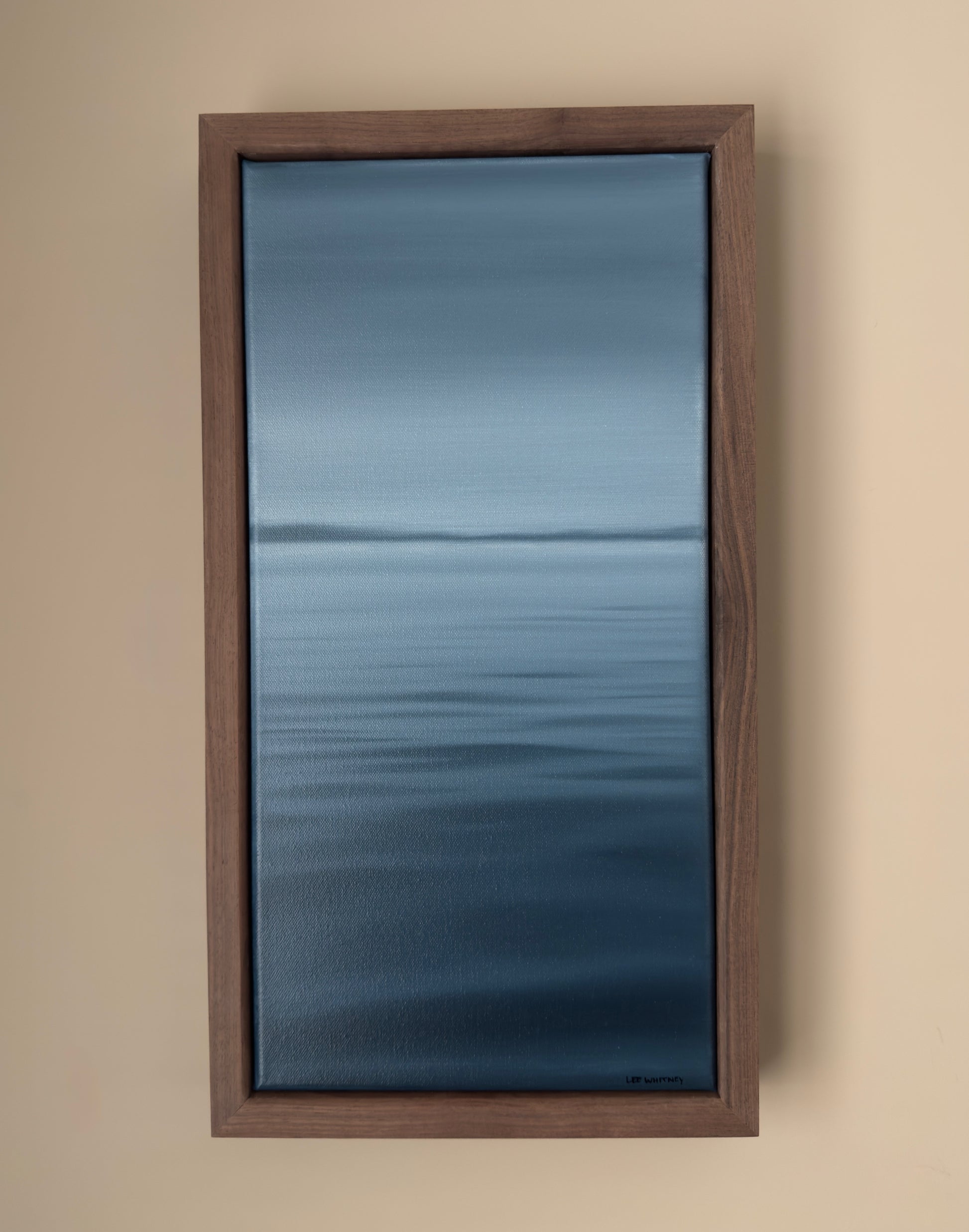 Framed artwork of a blue abstract waterscape on a beige wall